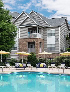Charming apartment complex with a spacious pool area featuring stylish lounge chairs and vibrant yellow umbrellas.