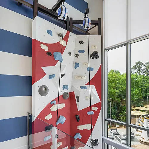 Indoor climbing wall with bright colors near a large window in a luxury apartment complex.