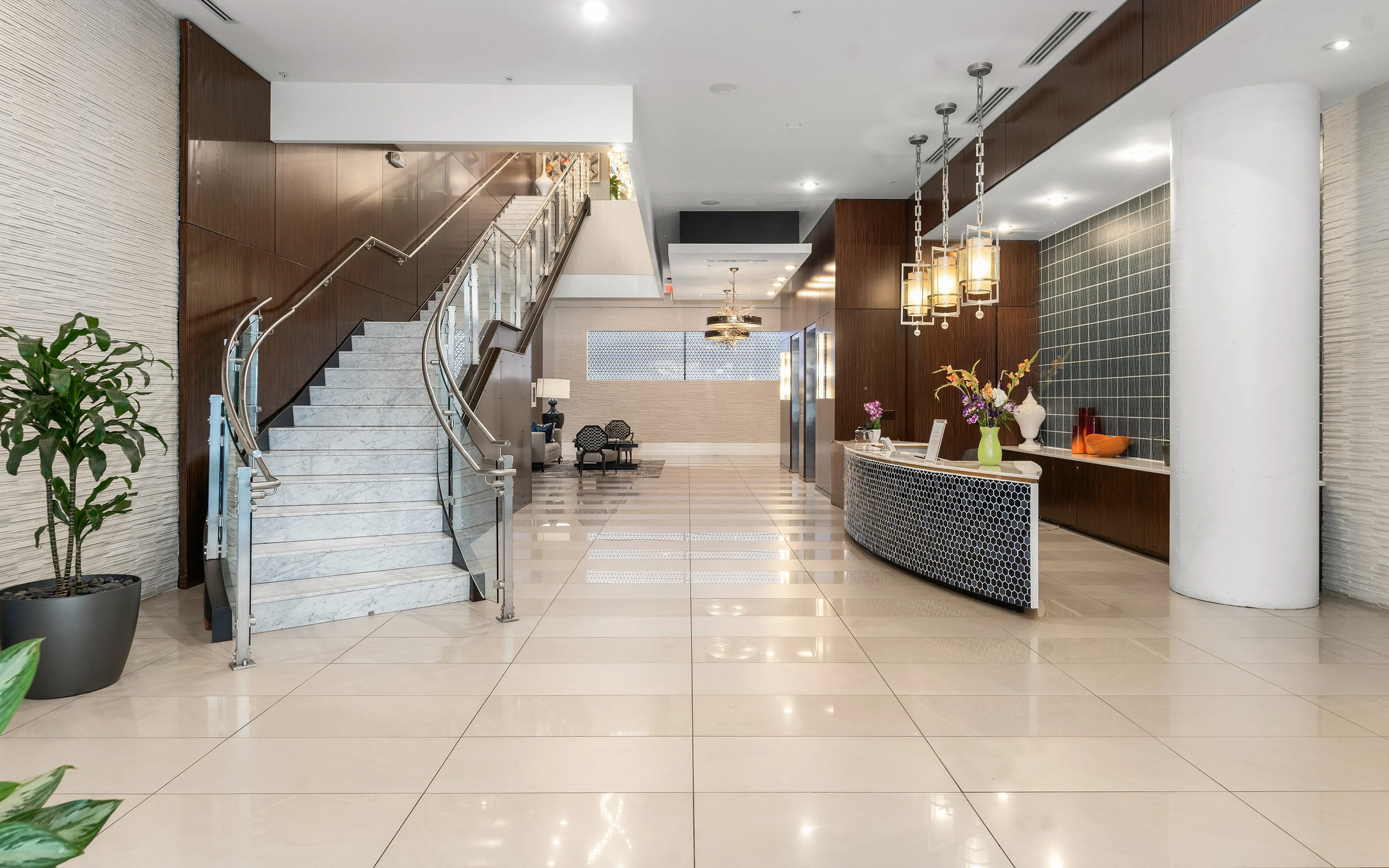 Spacious modern apartment lobby with elegant marble staircase, stylish reception desk, and chic seating area.
