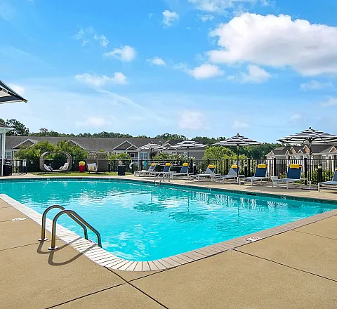 Outdoor swimming pool with sun loungers, umbrellas, and scenic views of the apartment complex.