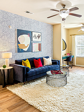 Stylish living room with modern decor and cozy ambiance featuring a plush blue sofa, colorful cushions, and patterned wallpaper.