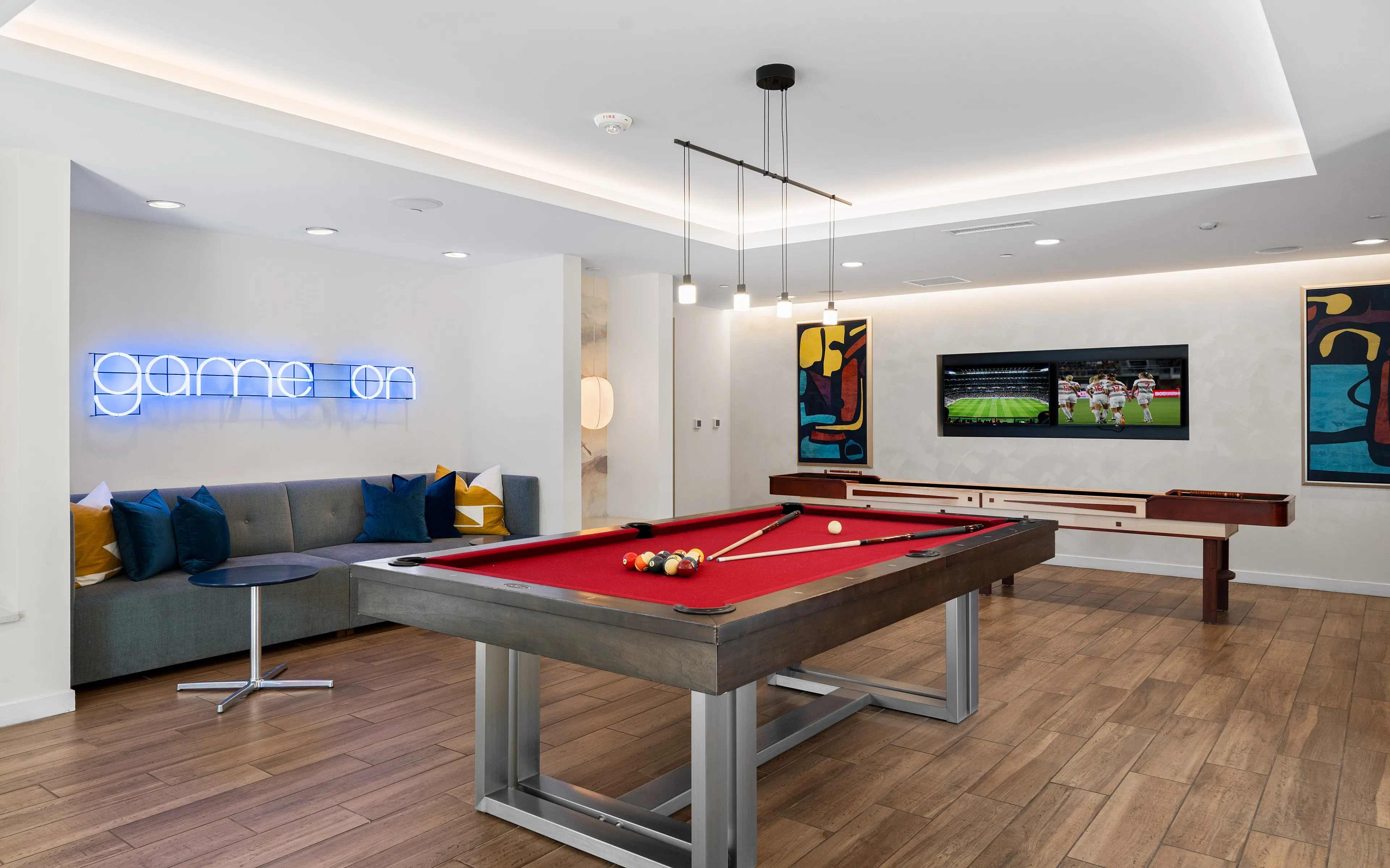 Contemporary game room with a red billiards table, sleek furniture, and a neon 'game on' sign