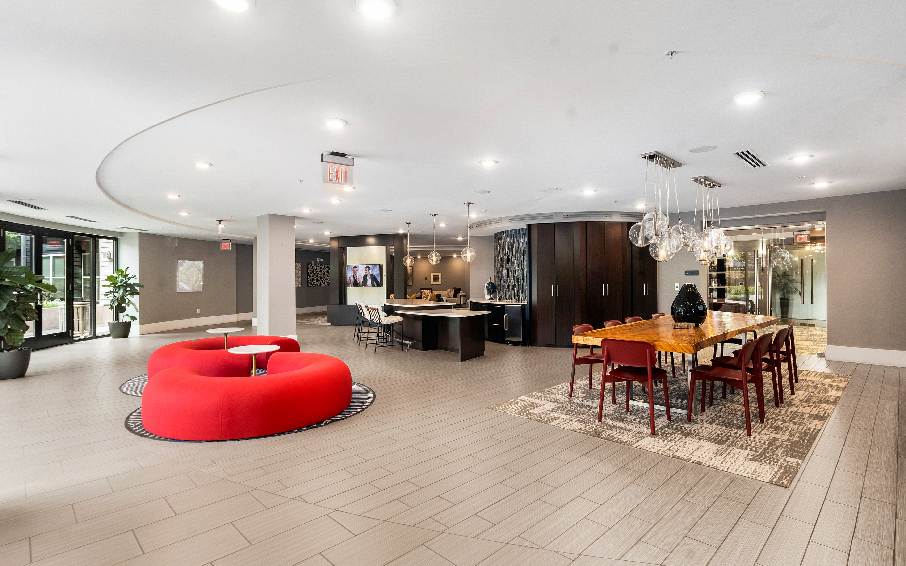 Spacious apartment lounge with stylish furniture, including a red circular couch and wooden dining table, complemented by contemporary lighting and lush plants.