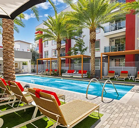 Modern apartment complex with palm trees and swimming pool in a sunny courtyard.