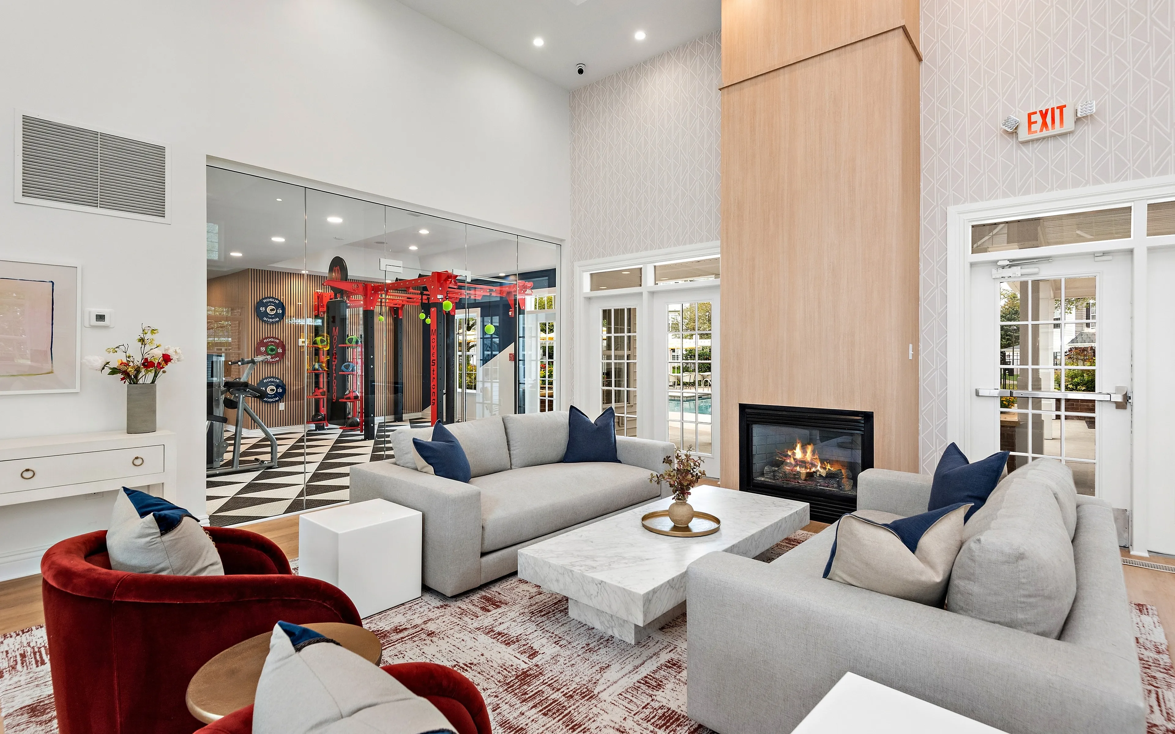 Modern living area with elegant gray sofas, a marble coffee table, and a cozy fireplace, complemented by a vibrant fitness center in the background.