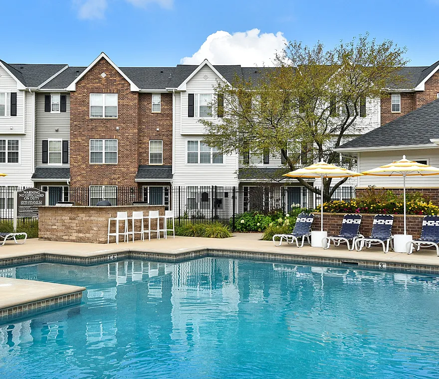 Inviting apartment complex with a sparkling pool, stylish loungers, and umbrellas for a perfect relaxation spot.