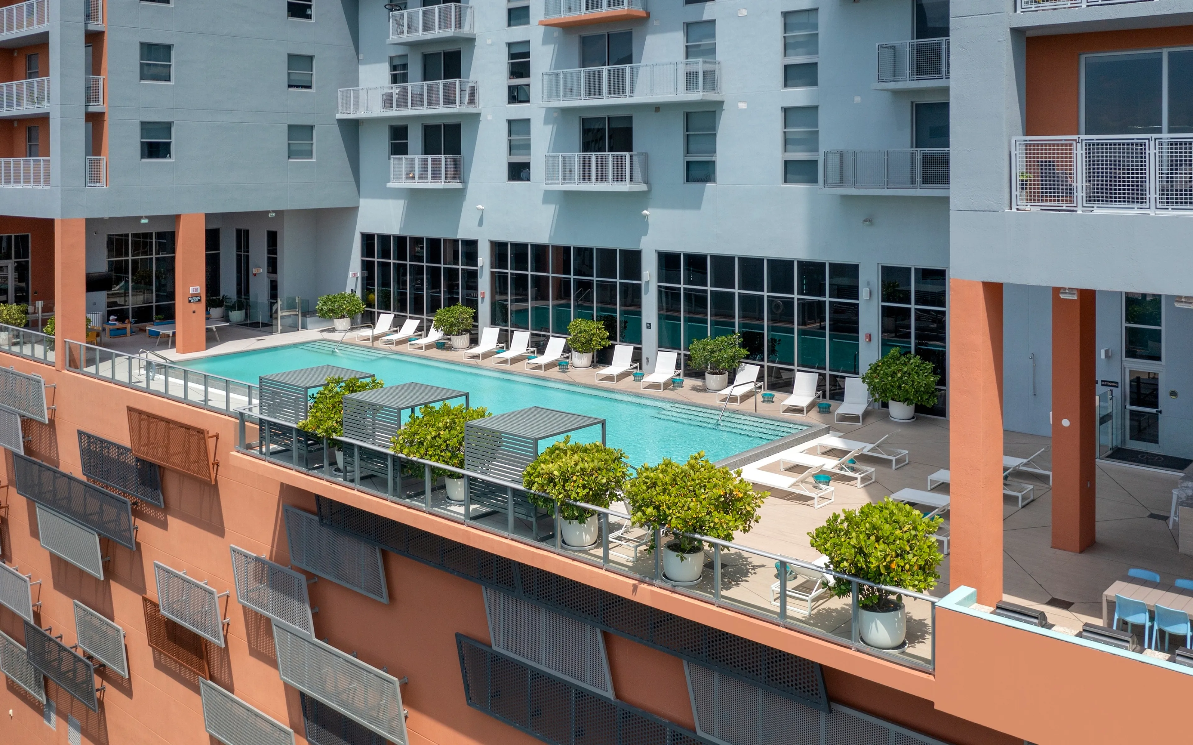 Luxurious apartment complex featuring a sleek outdoor pool, modern sun loungers, and vibrant greenery, offering an exclusive resort-style living experience.