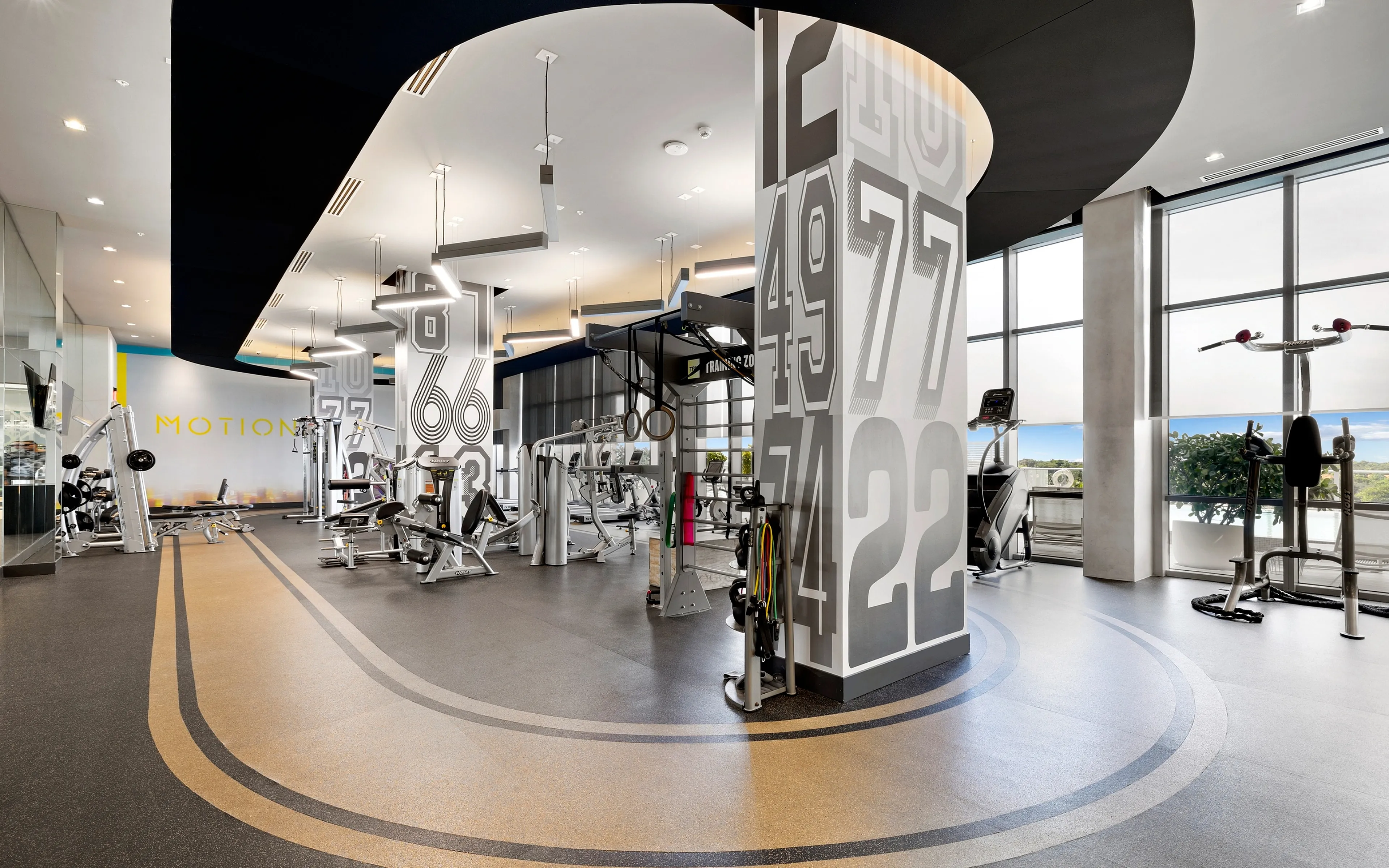 Modern gym with sleek equipment, artistic wall designs, and expansive windows offering scenic views, ideal for dynamic workouts and fitness activities.