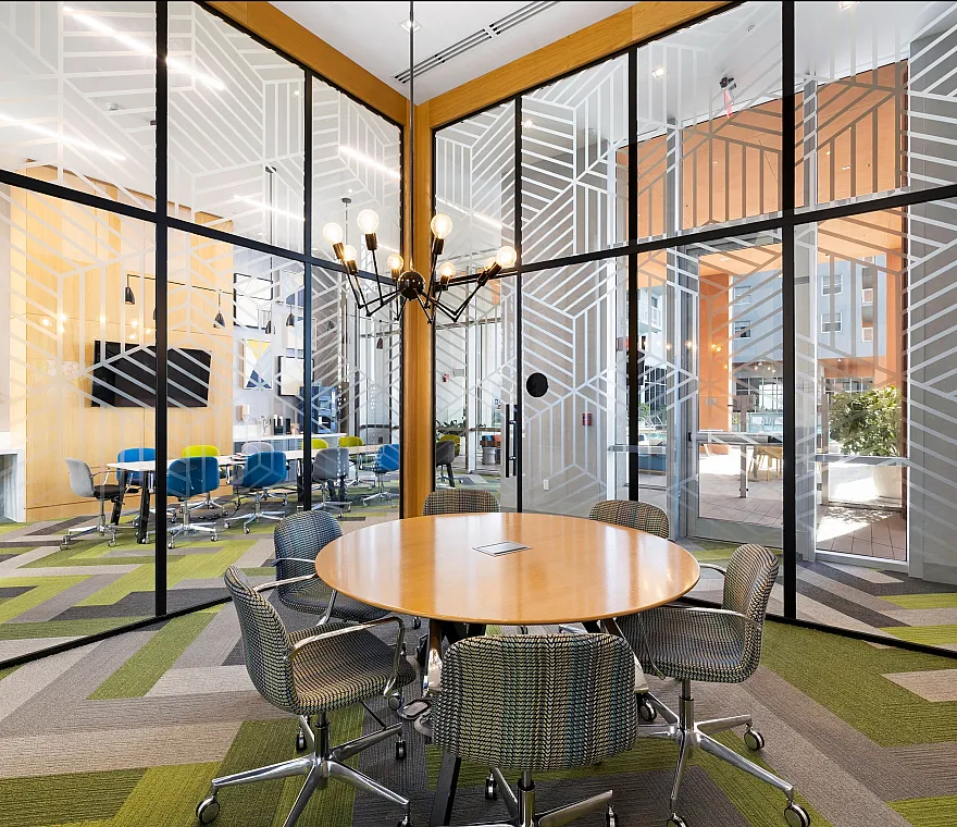 Modern conference room with sleek glass walls, geometric patterns, stylish round table, and colorful chairs creating a dynamic workspace.