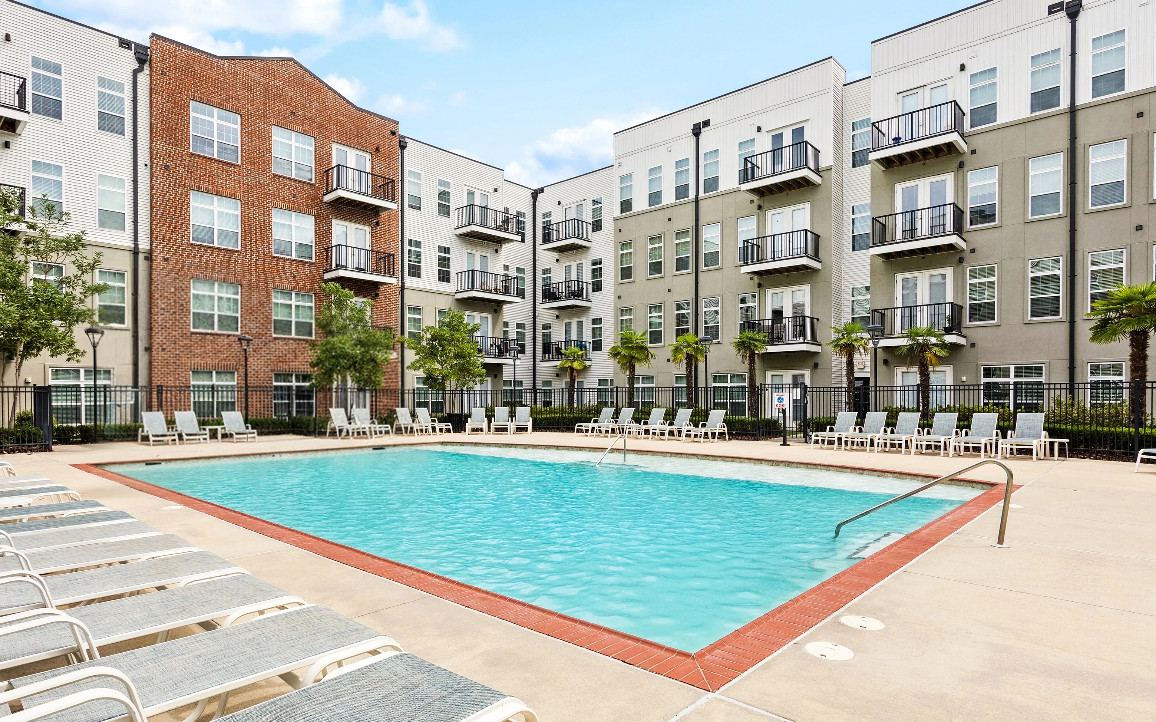 Elegant apartment complex with a resort-style swimming pool surrounded by lounge chairs and lush landscaping.