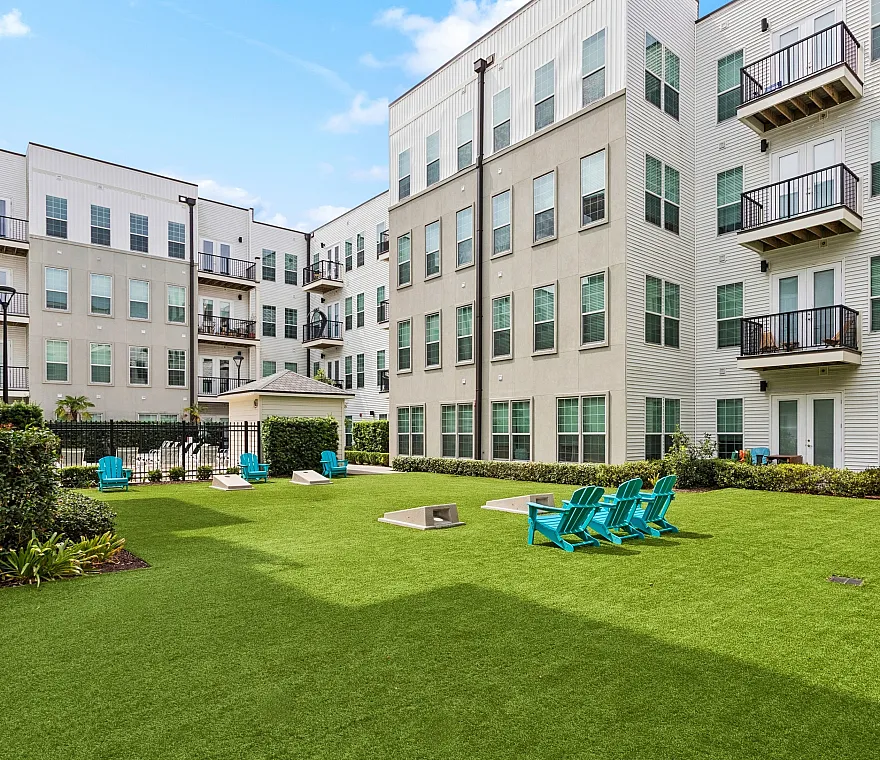 Modern apartment complex with a vibrant green courtyard featuring relaxing blue chairs and lush landscaping.
