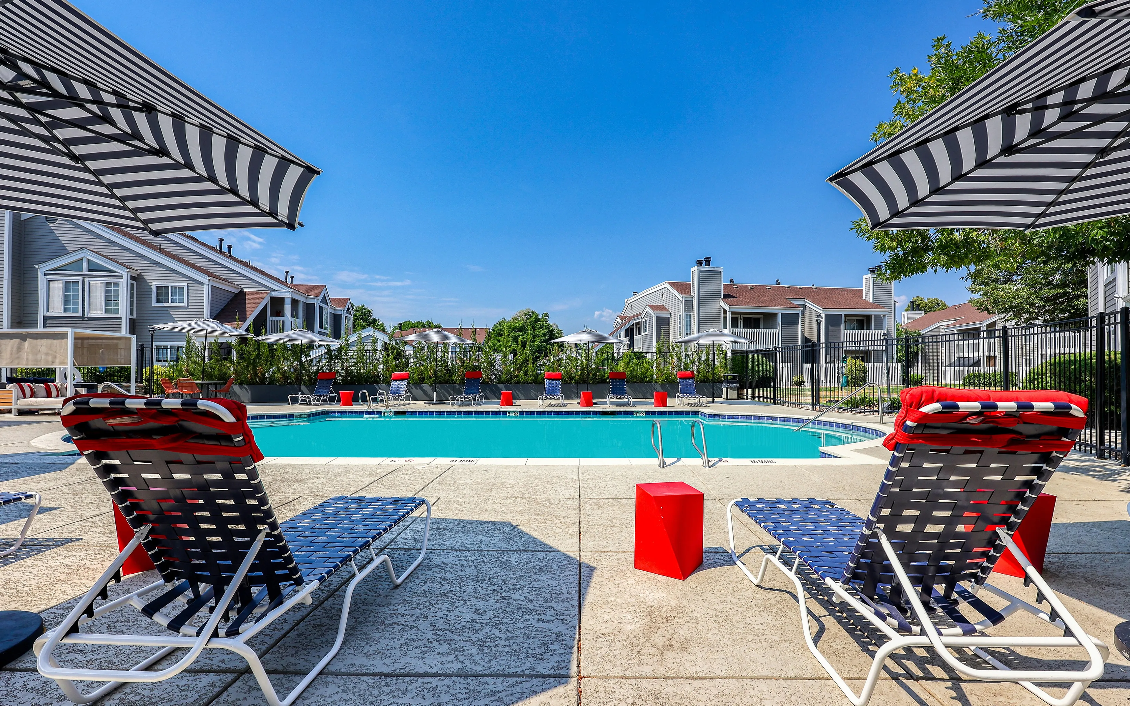 Inviting community pool area with stylish lounge chairs and umbrellas, surrounded by modern townhouses under a clear blue sky.