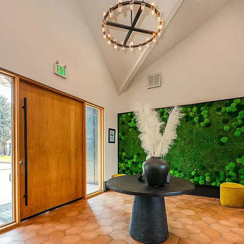 Inviting apartment entryway with a modern chandelier, hexagonal tiled floor, and vibrant green plant wall art.