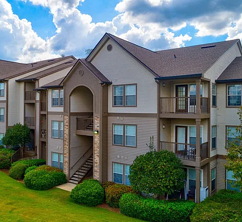 Charming multi-story apartment building with inviting balconies, surrounded by lush greenery and bright blue skies.