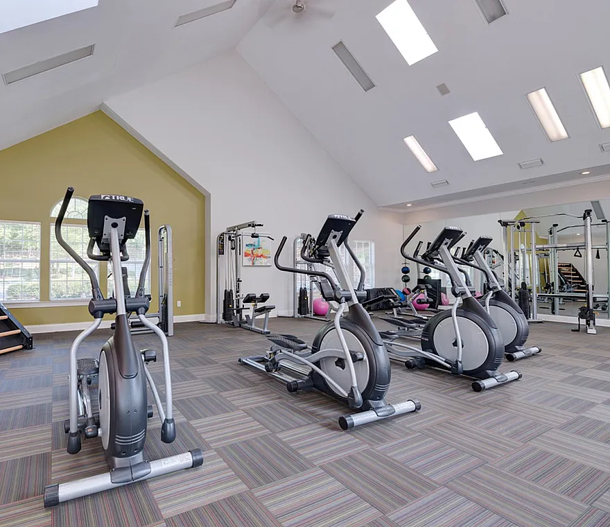 Spacious and modern fitness center featuring elliptical machines, strength training equipment, and natural lighting from skylights.