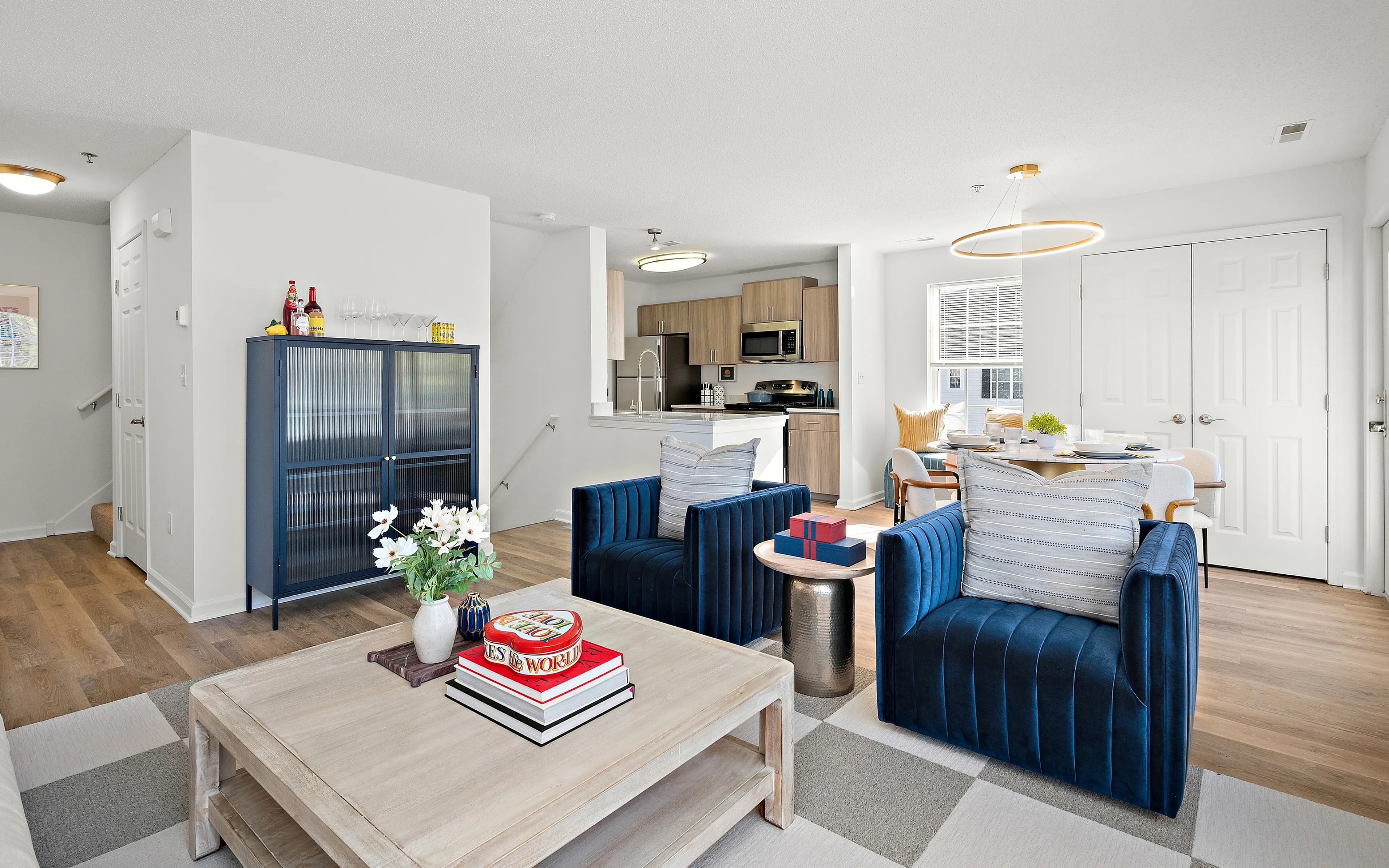 Inviting open-concept living area with stylish blue velvet chairs, modern kitchen, and elegant dining space filled with natural light.