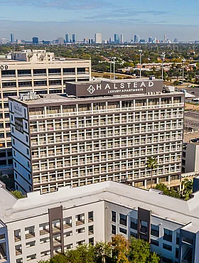 Stunning aerial view of Halstead Luxury Apartments, showcasing modern architecture surrounded by lush greenery, with a vibrant city skyline in the background.