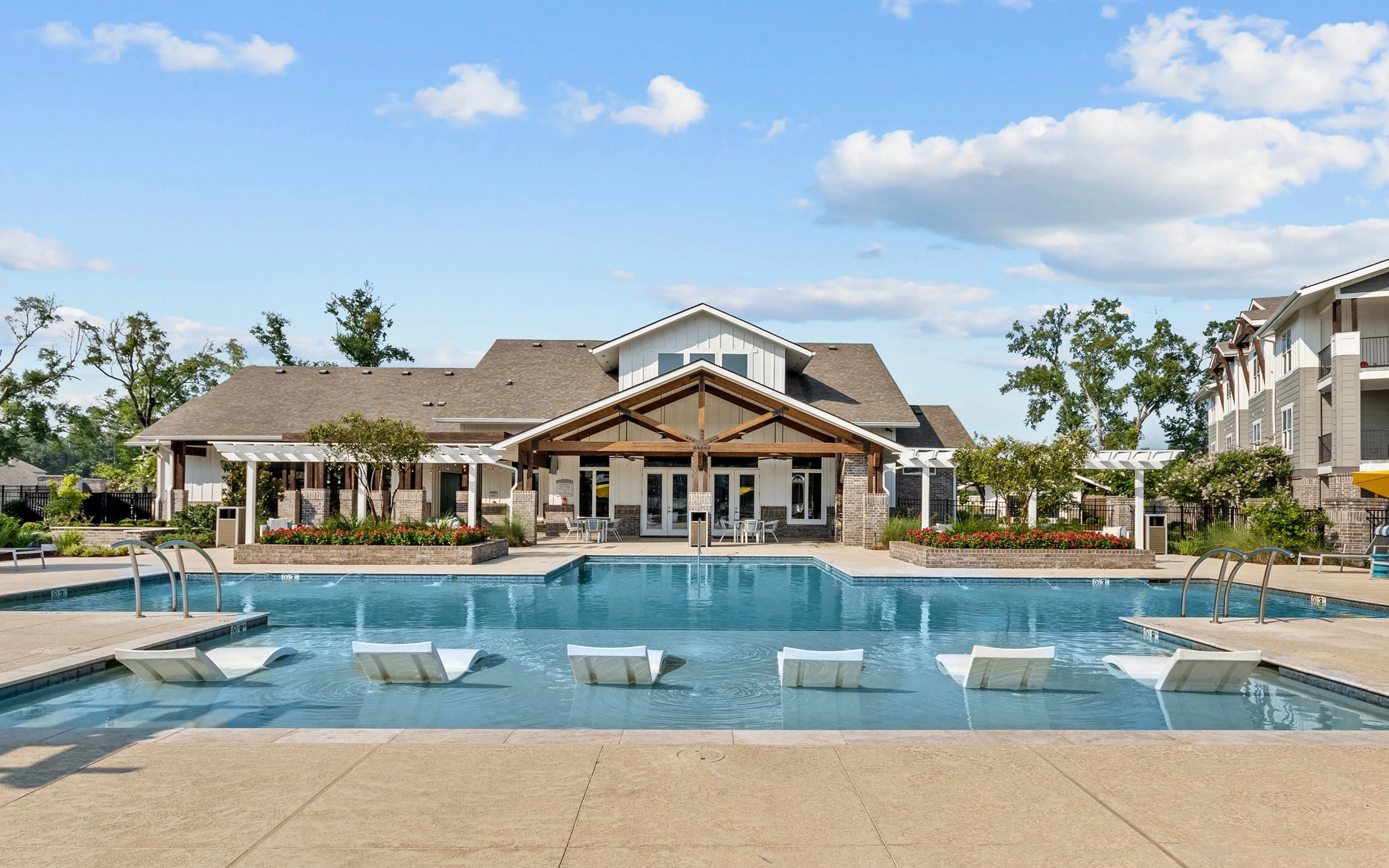 Luxurious apartment community with a sparkling pool, inviting lounge chairs, and vibrant umbrellas under a clear blue sky.