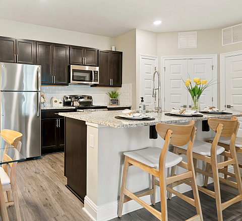 Bright, modern kitchen featuring a stainless steel fridge, elegant granite countertops, and inviting breakfast bar with wooden stools, complemented by a cozy dining area with vibrant orange chairs.