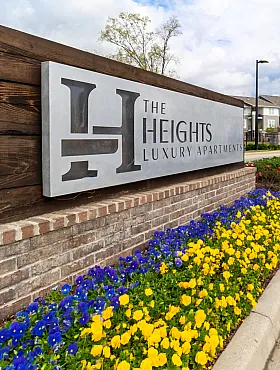 Inviting entrance to The Heights Luxury Apartments, showcasing a modern sign with vibrant flowers and elegant residential buildings in the background.
