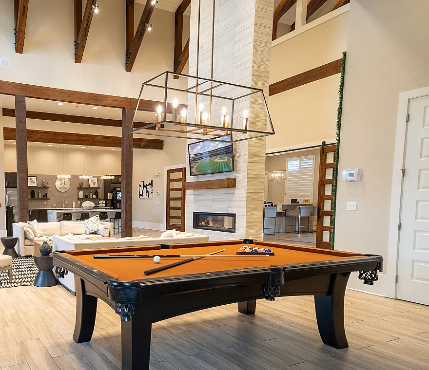 Elegant open-concept living space featuring a chic billiard table, modern high ceilings with exposed beams, cozy seating area, and stylish fireplace, perfect for entertaining.