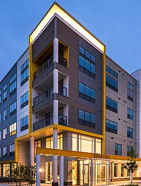 Modern apartment complex illuminated at dusk, showcasing sleek architecture with large windows and inviting balconies.
