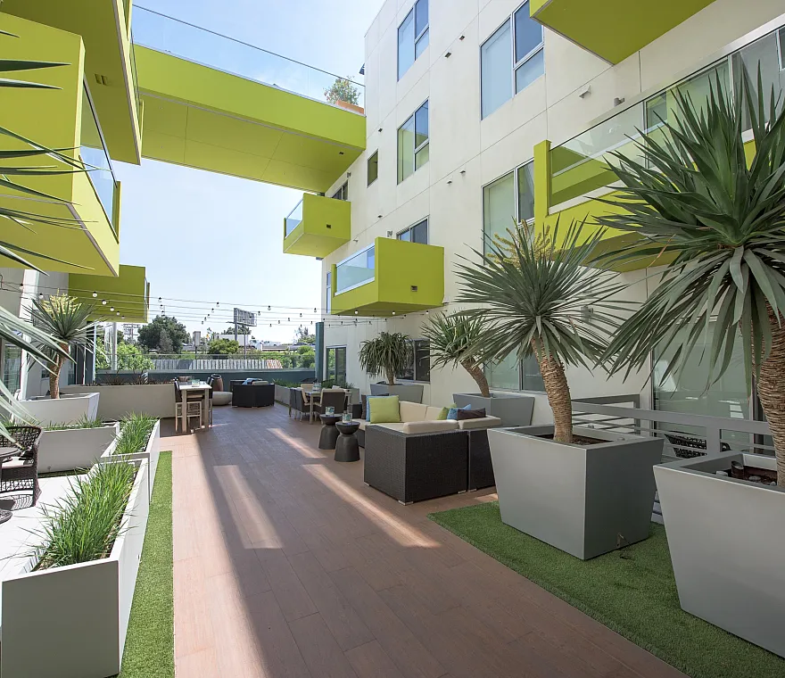 Modern apartment complex with vibrant green balconies, stylish outdoor seating, and lush tropical plants.
