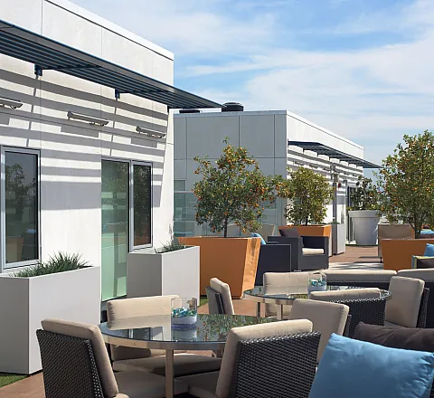 Luxurious rooftop terrace with modern seating arrangements, lush greenery, and a stunning glass railing offering panoramic views.
