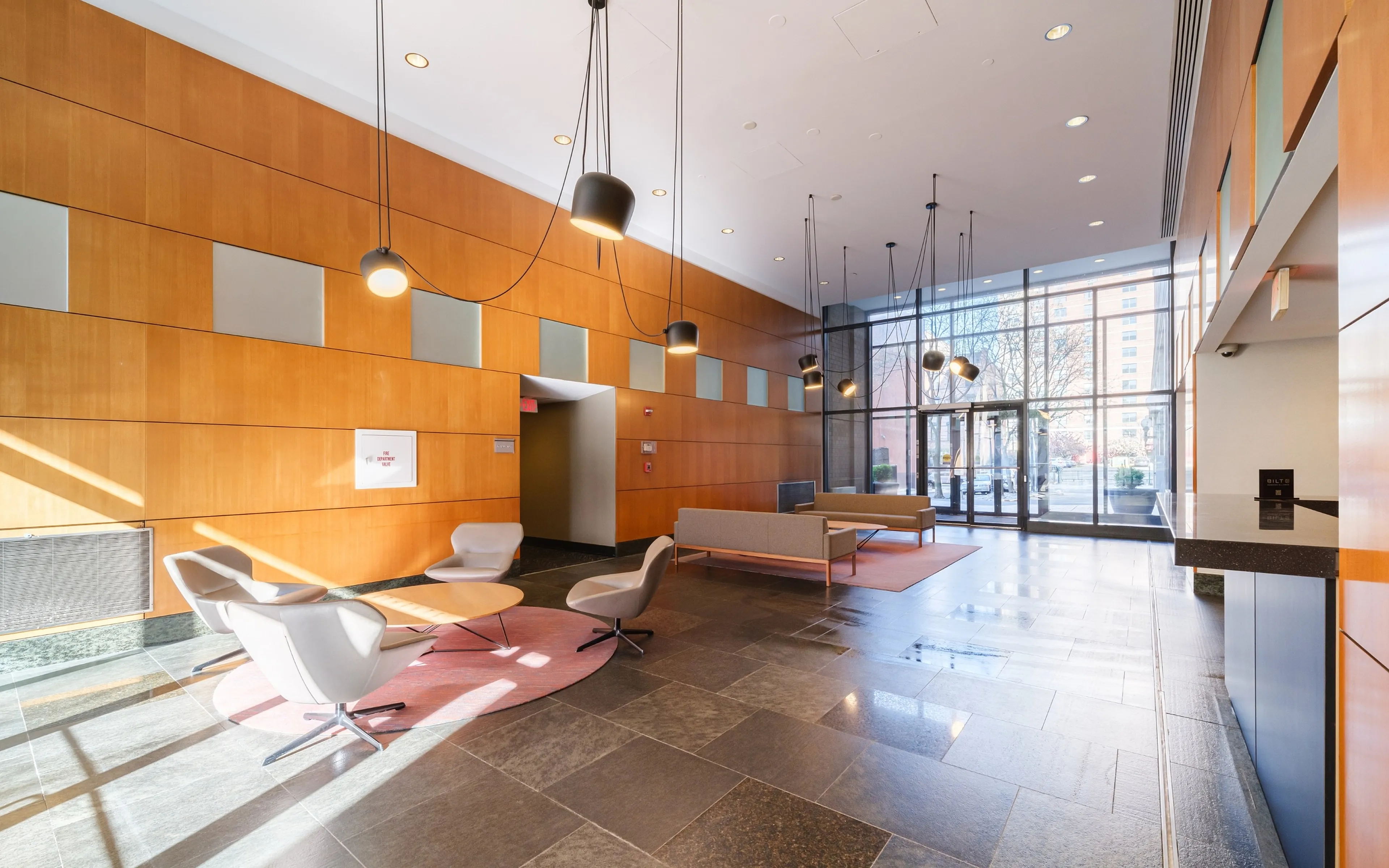 Bright and modern apartment lobby featuring elegant lighting, sleek seating area, and expansive windows offering city views.