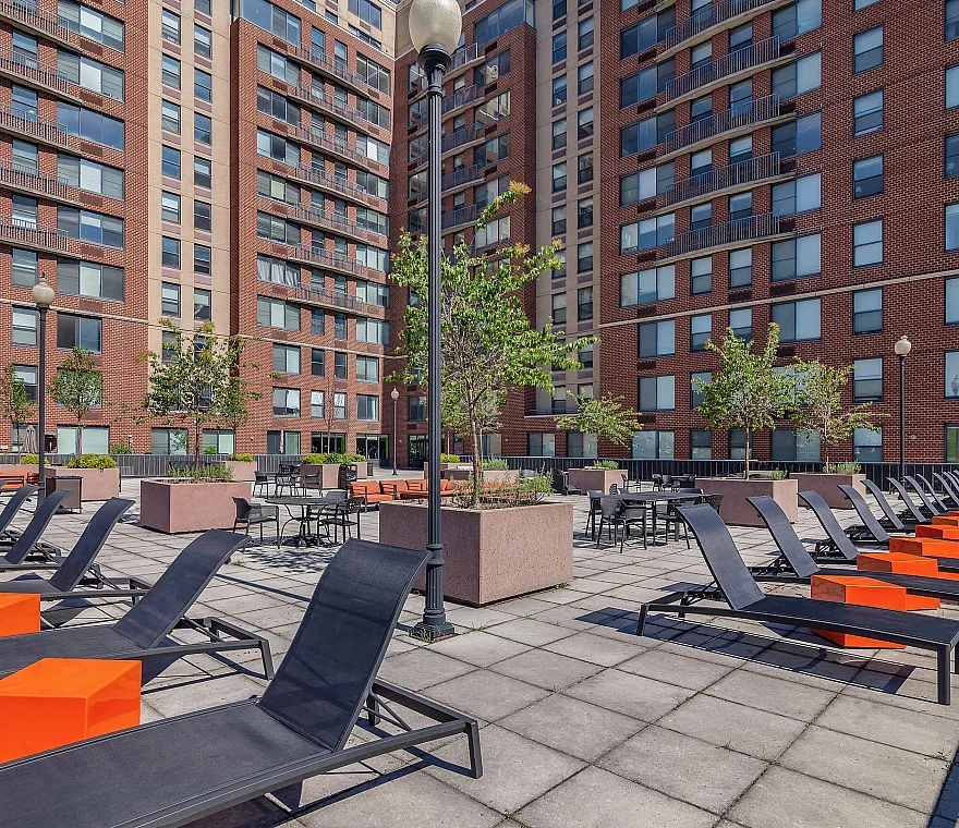 Vibrant outdoor terrace in an upscale apartment building, featuring stylish lounge chairs and elegant dining areas amidst lush greenery.