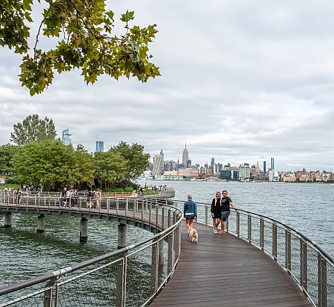 Charming waterfront promenade with lush greenery and stunning skyline views, perfect for a leisurely stroll.