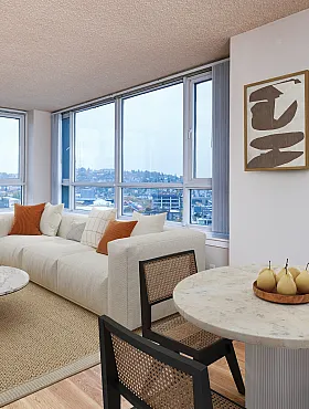 Bright and airy living room with expansive city views, featuring a modern white sofa, elegant marble coffee table, and cozy dining area with stylish decor.
