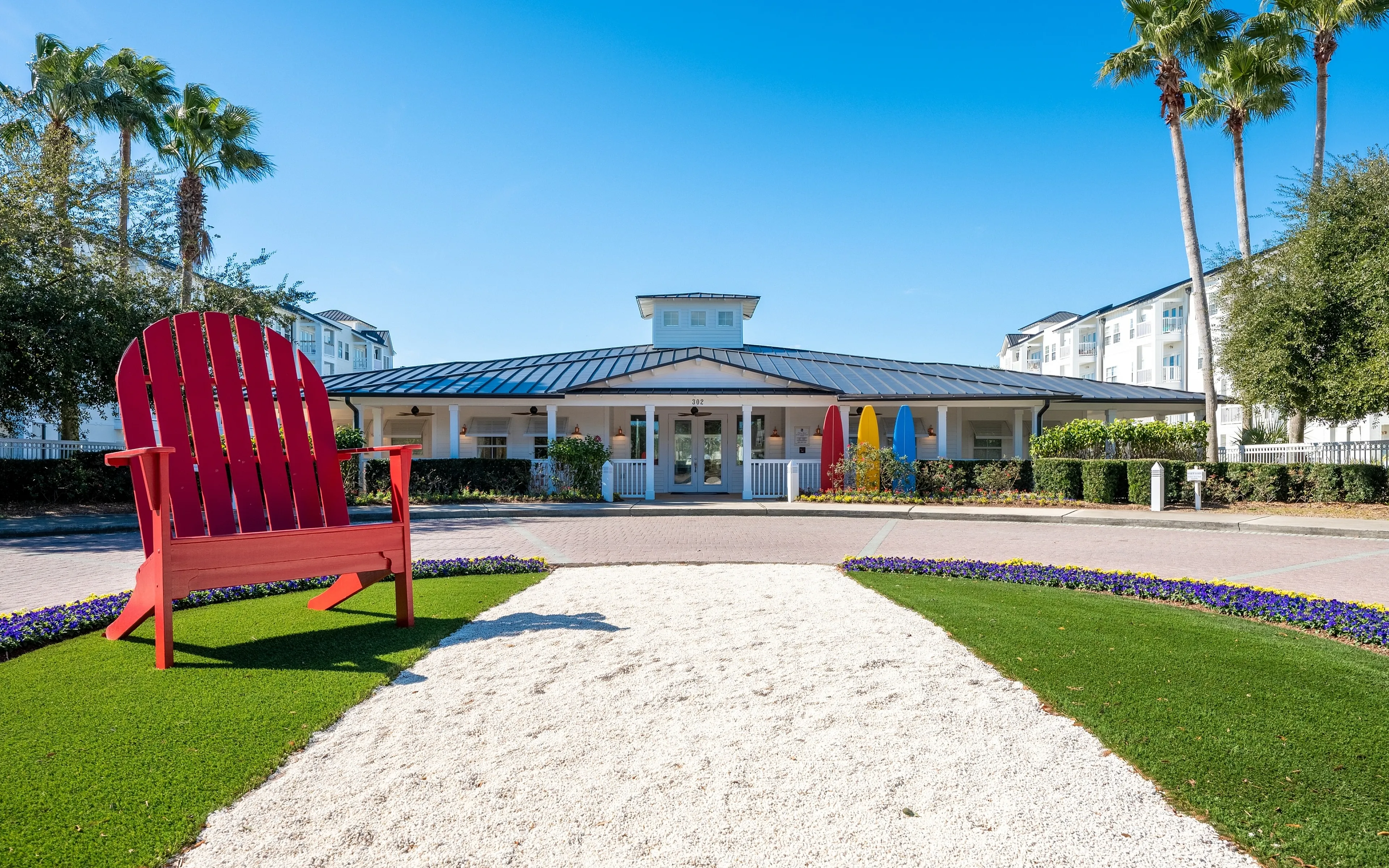 Inviting apartment entrance with vibrant landscape, featuring a charming red chair and colorful surfboards under the clear blue sky.