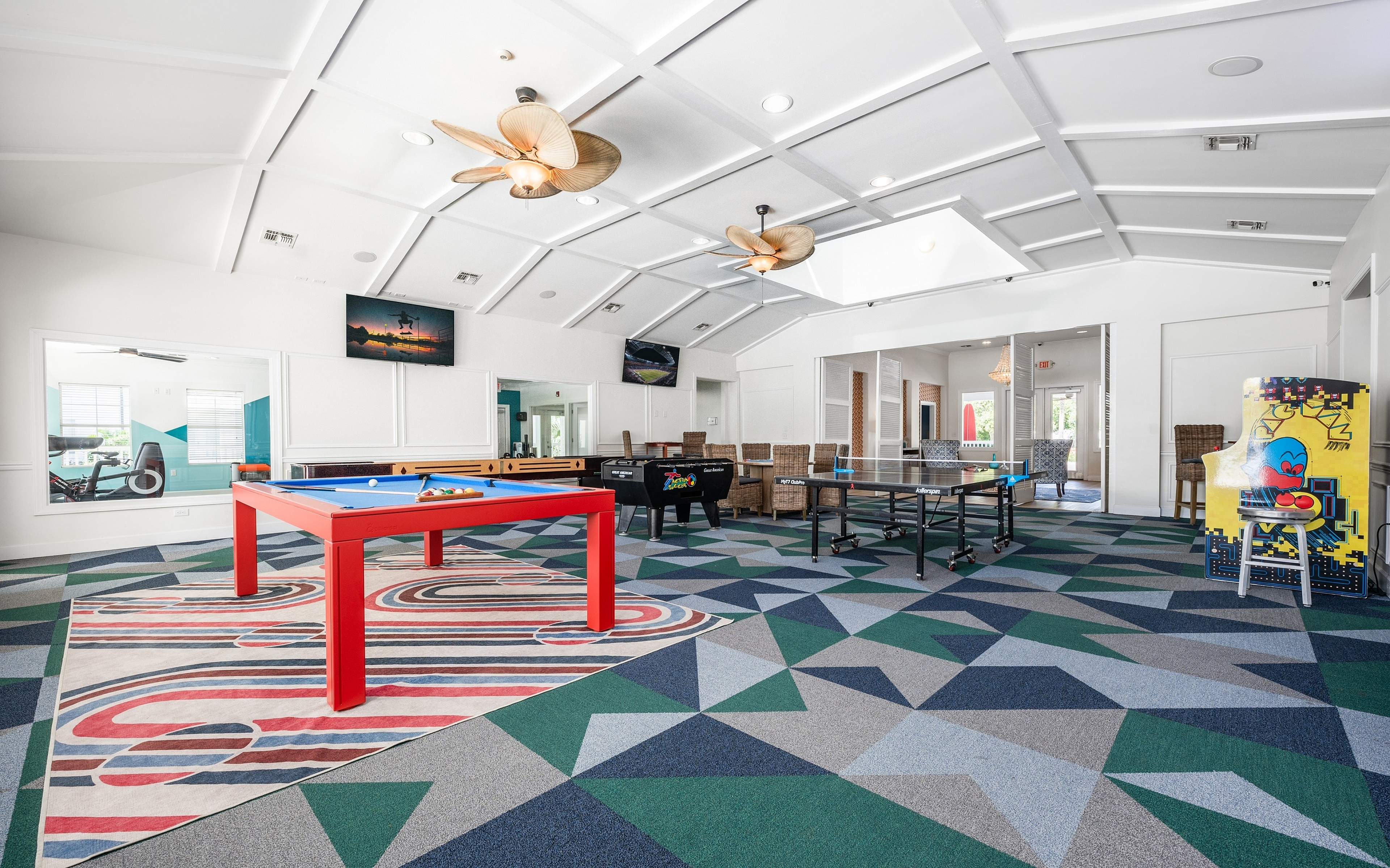 Vibrant recreation room featuring a modern gaming area with a pool table, ping pong, and arcade games under stylish ceiling fans and geometric carpet design.