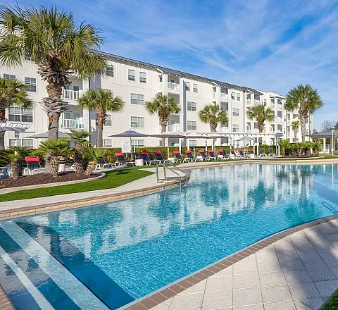 Luxurious apartment complex with a stunning resort-style swimming pool surrounded by lush palm trees and modern architecture, perfect for relaxation and leisure.