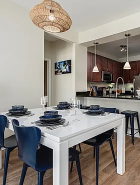 Chic open-concept dining and kitchen area featuring a sleek white dining table with modern blue chairs, stylish lighting, and elegant wood flooring.