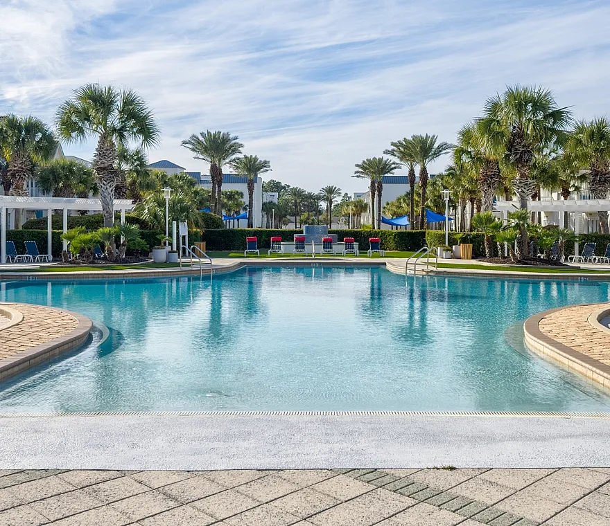 Luxurious apartment complex featuring a sparkling pool surrounded by lush palm trees and modern lounge areas.