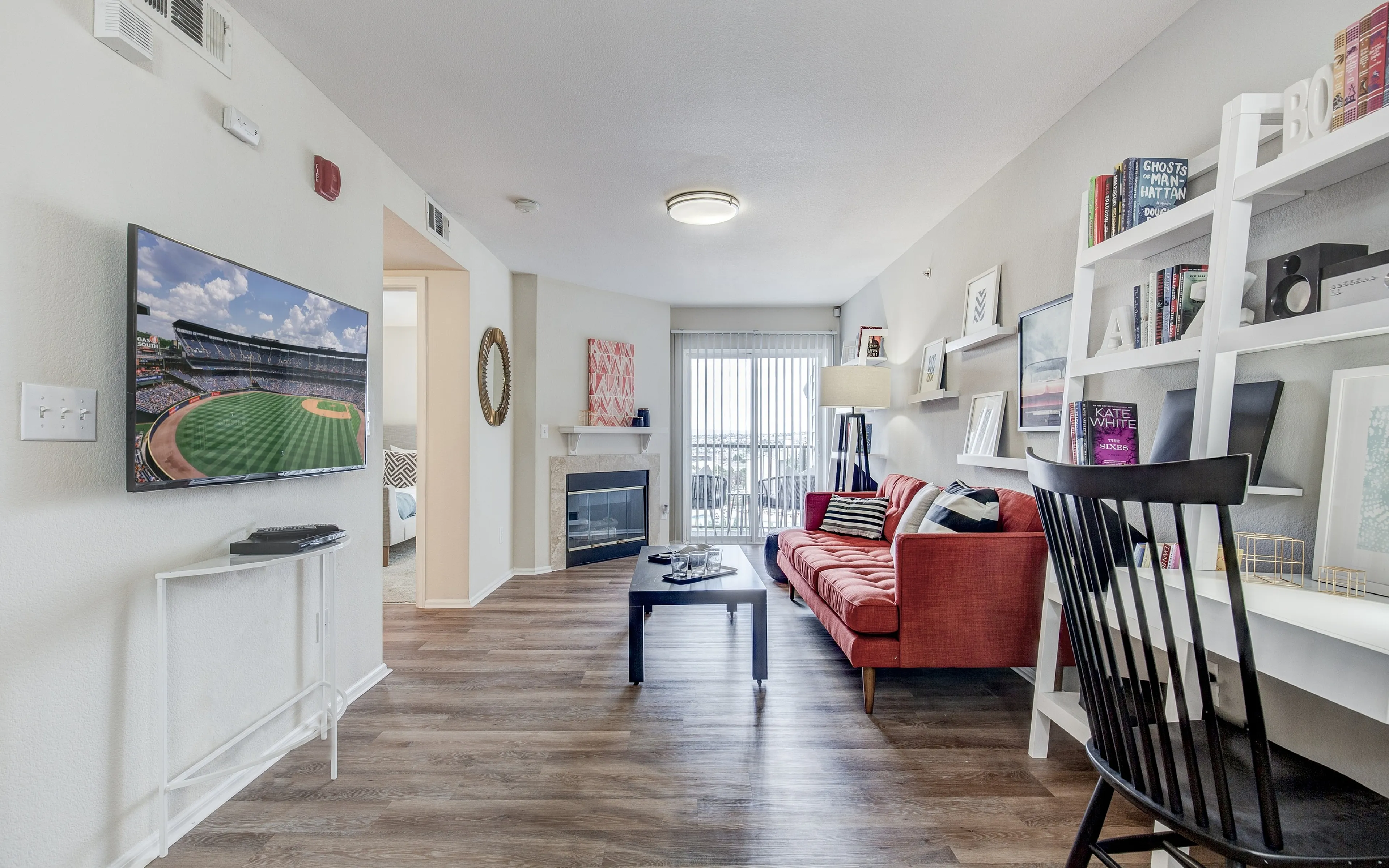 Inviting living room with a modern red sofa, wall-mounted TV, and cozy fireplace, featuring elegant decor and bright, natural light from large windows.