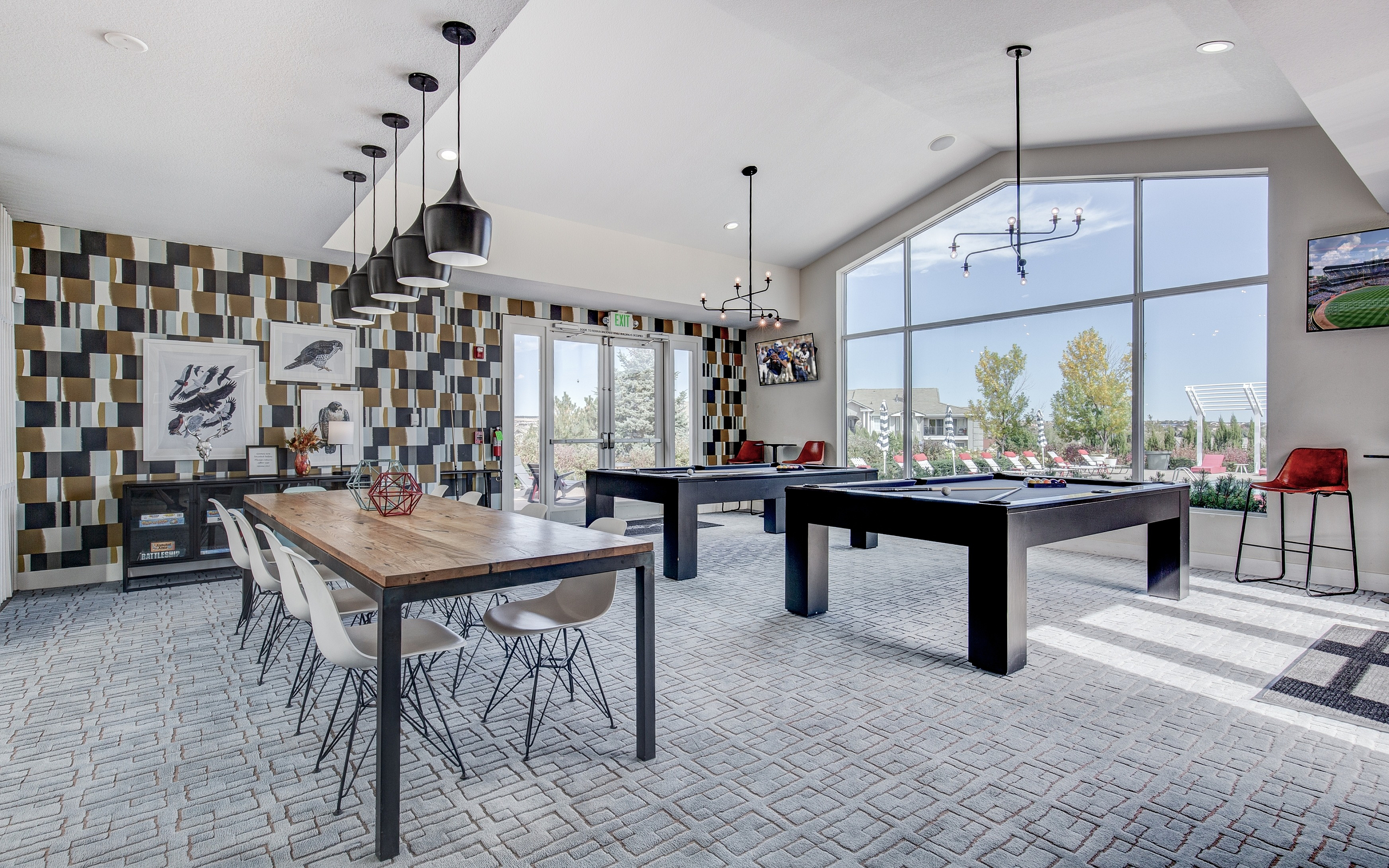 Inviting game room with modern pool tables, stylish pendant lighting, and expansive windows offering a scenic outdoor view.