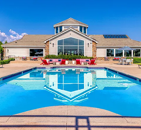Luxurious apartment complex featuring a sparkling blue pool, sun loungers, and stylish clubhouse with scenic views, perfect for relaxation.