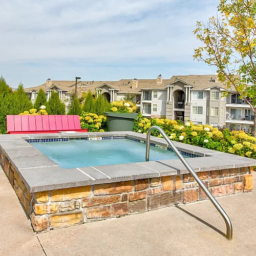 Charming outdoor patio featuring a cozy hot tub surrounded by lush greenery and vibrant flowers, offering a tranquil retreat with scenic apartment views.