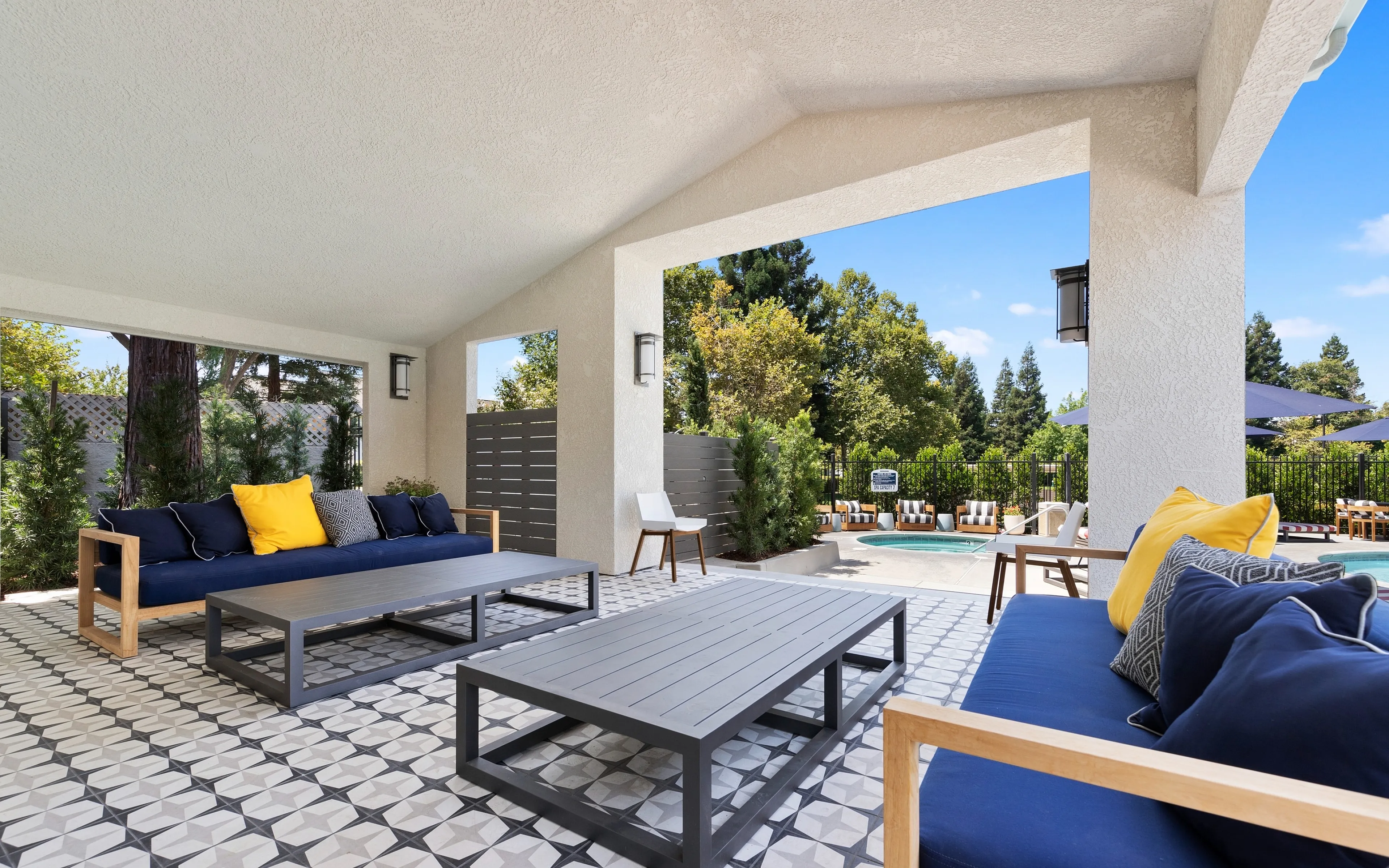Chic outdoor lounge with patterned flooring, modern furnishings, and a view of a sparkling pool and lush garden.