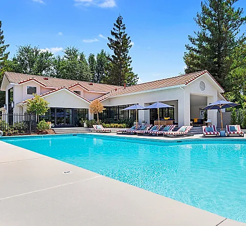 Luxurious community pool area with stylish loungers, umbrellas, and lush landscaping, offering a relaxing oasis for outdoor enjoyment.