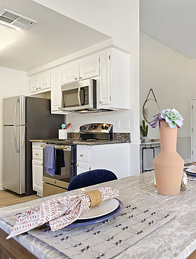 Elegant open-plan apartment featuring a modern kitchen, cozy living area with leather couch, and a beautifully set dining table.