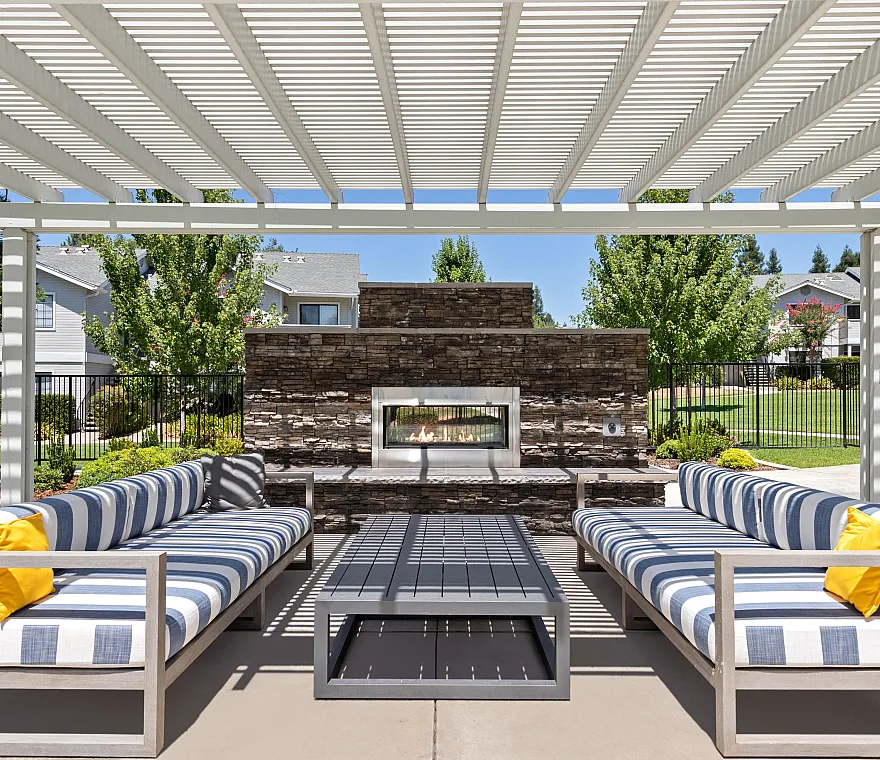 Chic outdoor patio with striped sofas and vibrant yellow accent pillows, featuring a modern stone fireplace under a stylish pergola.