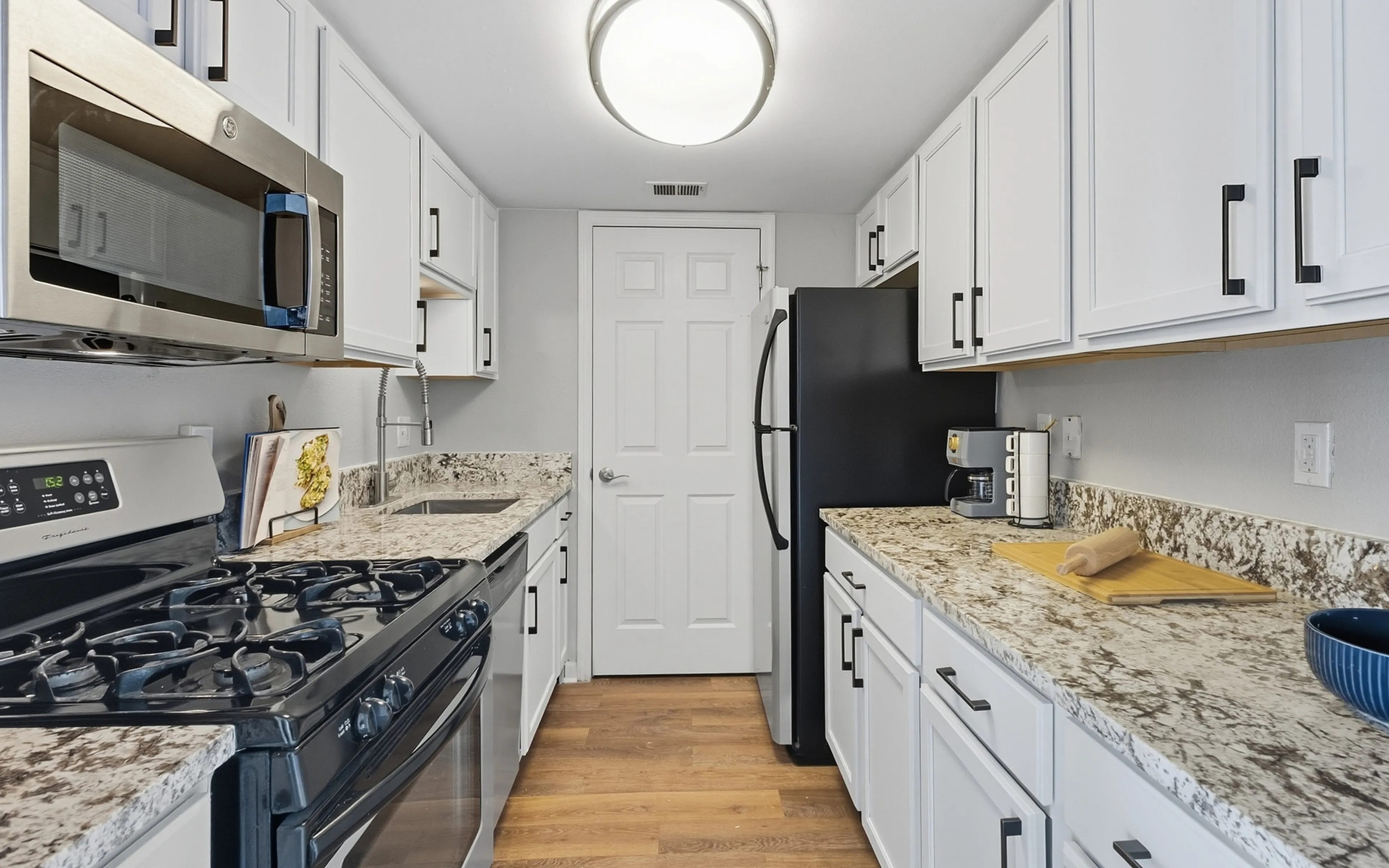 Modern kitchen with sleek white cabinets, granite countertops, and stainless steel appliances in a stylish apartment.