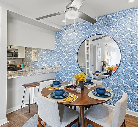 Chic dining area with vibrant blue wallpaper, a stylish round mirror, and a cozy table setting for four, perfect for intimate gatherings.