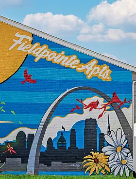 Vibrant mural at Fieldpointe Apartments featuring a red cardinal, St. Louis skyline, and colorful daisies, adding artistic flair to the community.