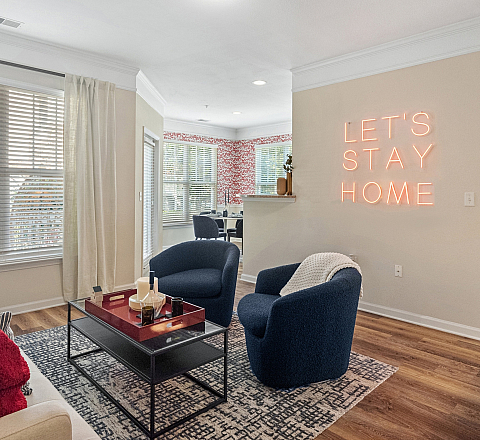 Inviting living room with modern furnishings, cozy blue chairs, and a neon 'Let's Stay Home' sign, perfect for relaxation and comfort.