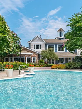 Luxurious apartment complex with a stunning outdoor pool surrounded by lush greenery and vibrant flowers.